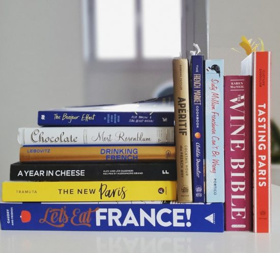 stack of books about French food and culture, including cookbooks and books on wine.