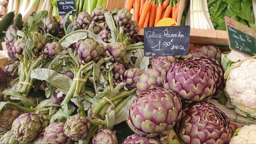 Artichokes, carrots, and various vegetables showcased at a vibrant market. Fresh produce galore!